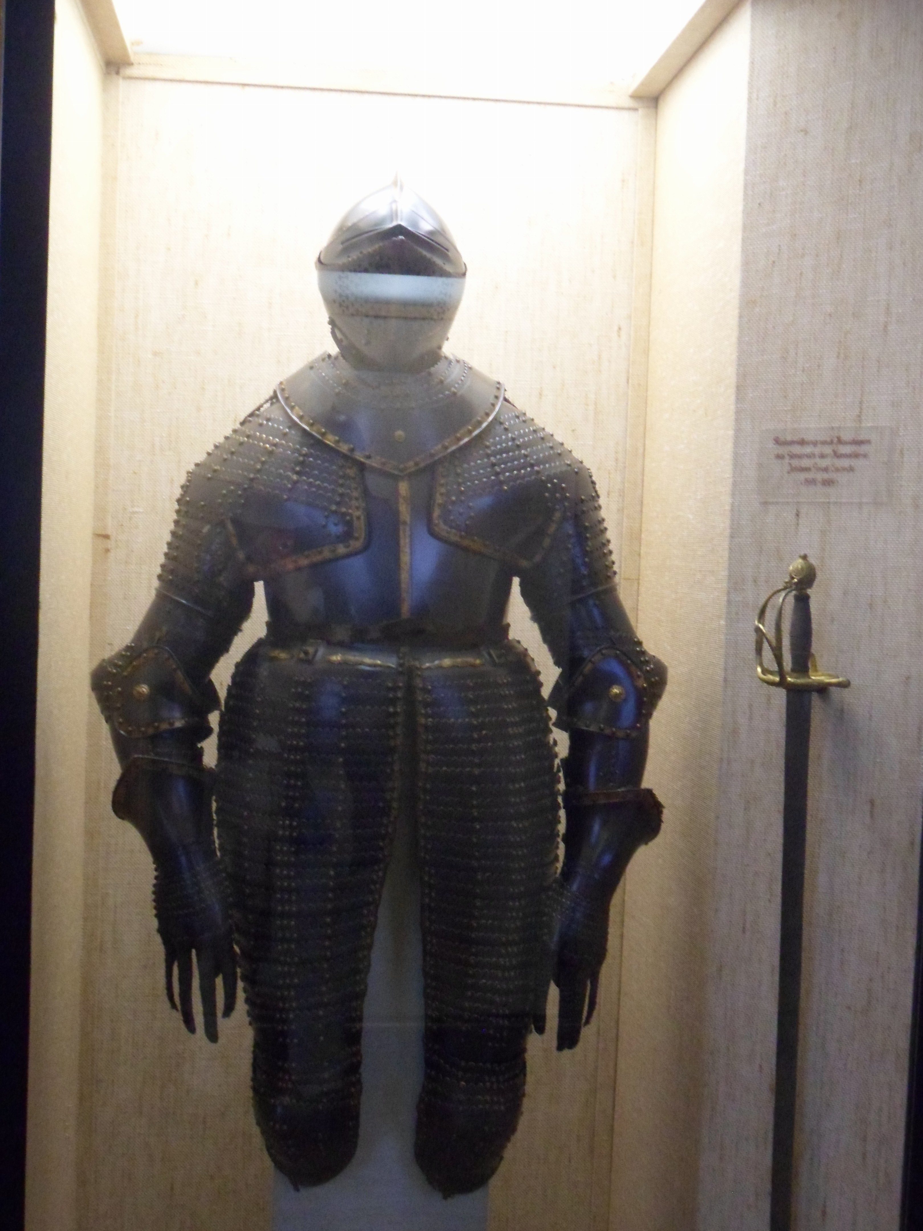 Suit of black plate armour with a closed helmet, articulated pauldrons, and tassets which flare at the hips and extend below the knees