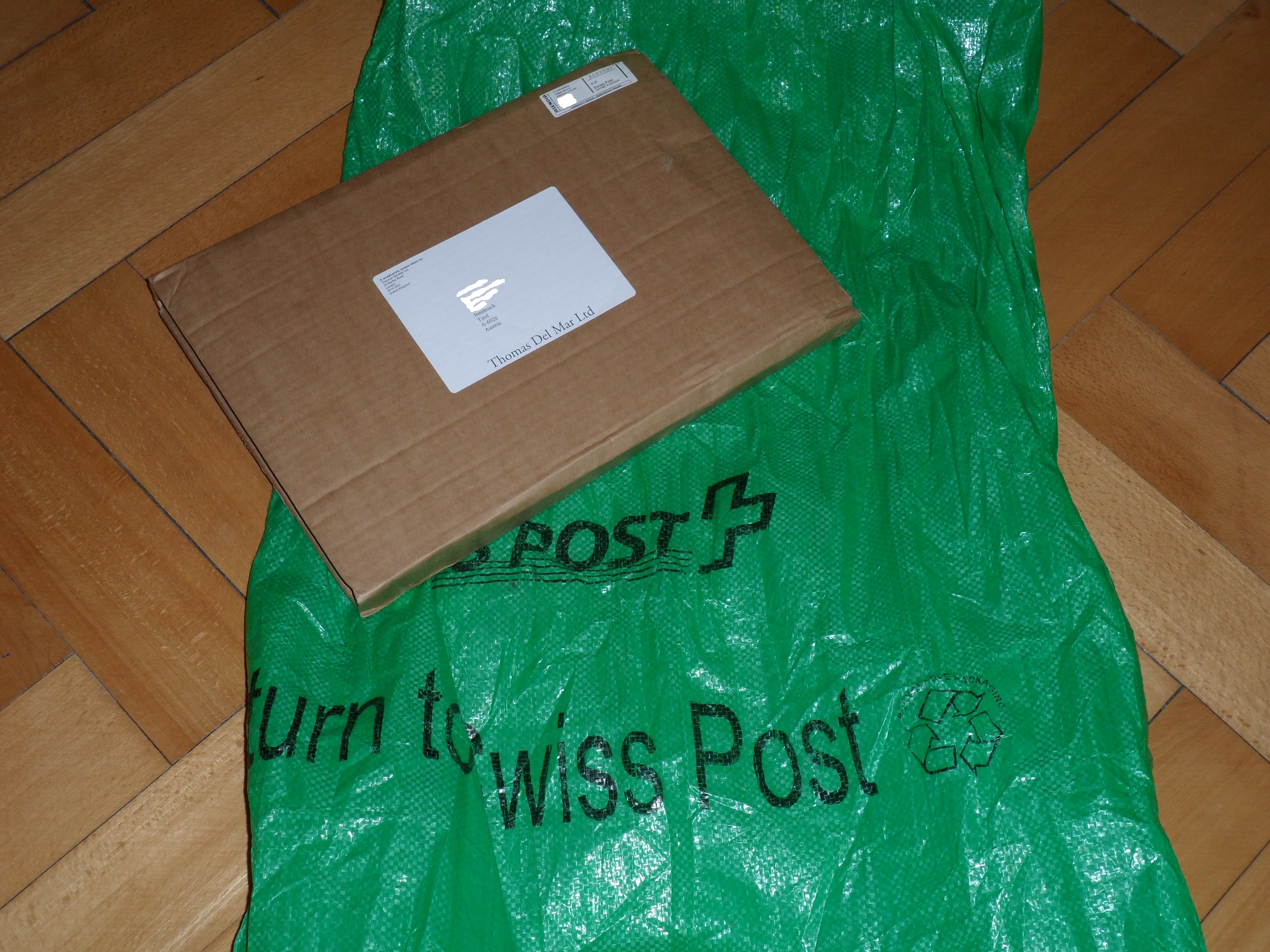 A folding slip of corrugated cardboard with a printed label carrying the address, over a green nylon bag a metre long and 50 cm wide labeled Swiss Post