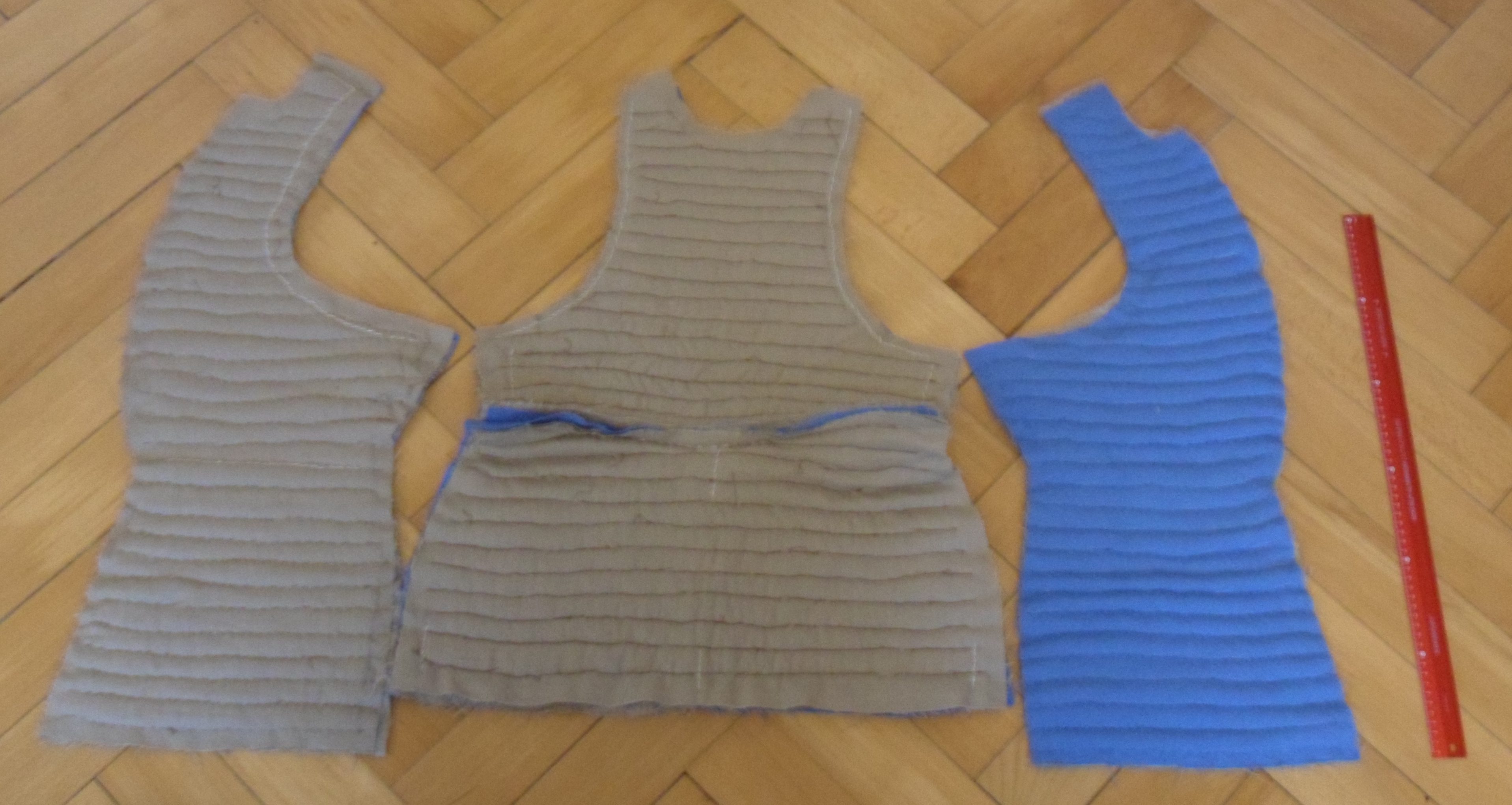 Components of a quilted doublet spread on the floor showing that one breast has blue cloth on the inside and one has brown there