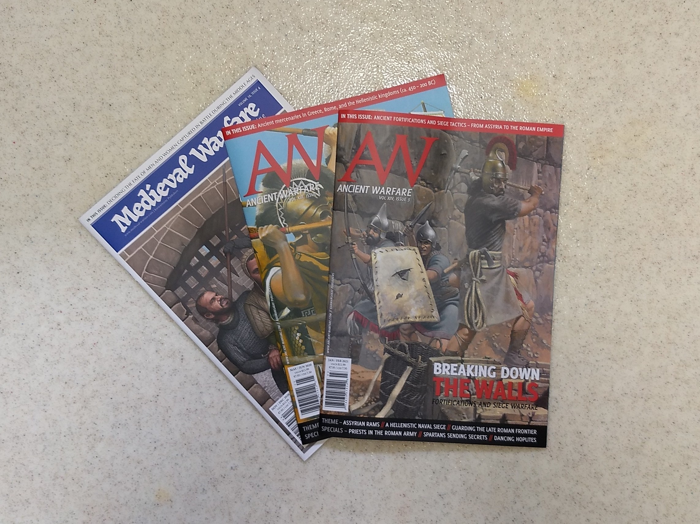 three issues of Ancient Warfare and Medieval Warfare magazine spread out on a textured linoleum surface