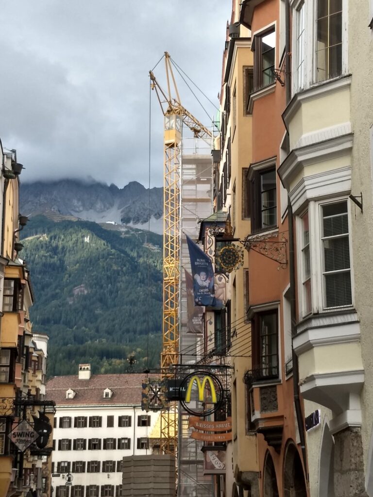 a photo of the Innsbrucker Altstadt with the Goldenes Dachl, the Nordkette, a construction crane, and the golden arches of McDonalds