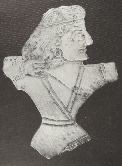 a photo of a piece of engraved and cut out white material with an archer in a kaftan with a headband and long curly hair drawing a bow to his right shoulder with three fingers bent around the string