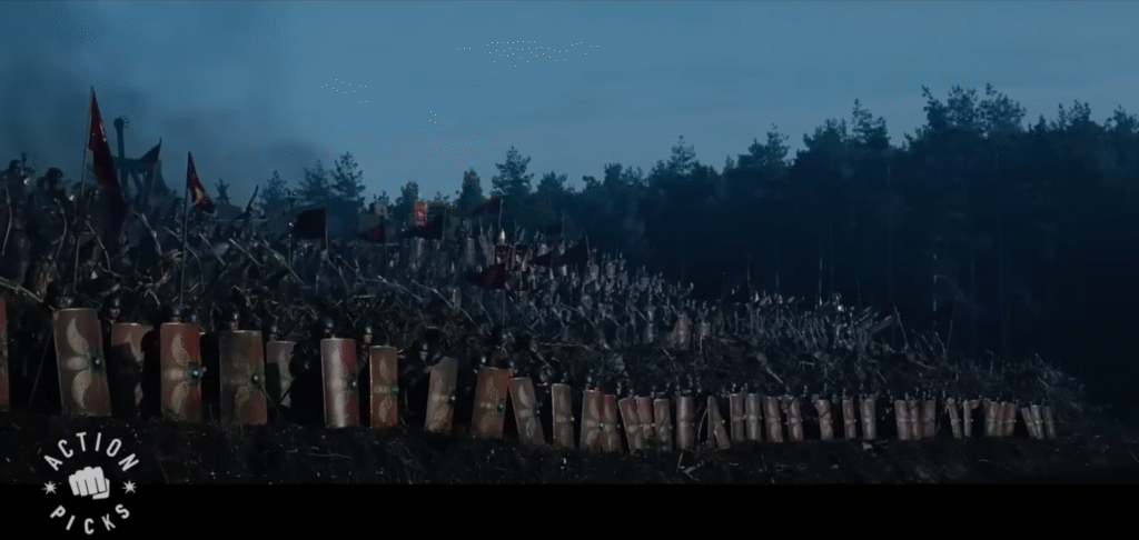 Maximus' army on a hill with catapults on the top, then archers, then infantry with long rectangular shields